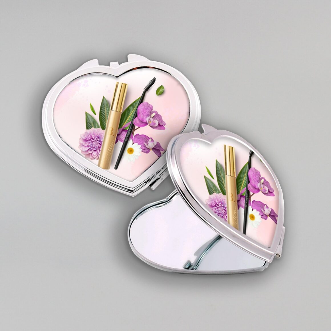A képen két szív alakú sminkes tükör látható. Az egyik nyitva van, a másik zárva. A tükör fedelén lila virágok és smink kellékek láthatóak, ezzel lett dekorálva a termék.